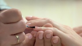 Beautician applying colorless varnish. Close up of woman applying transparent nail varnish to finger nails. Woman having nail manicure in beauty salon.