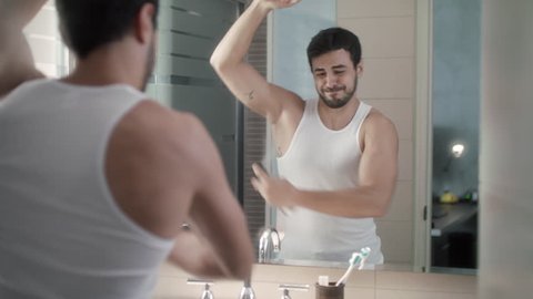 Young hispanic people and male beauty. White metrosexual man using spray deodorant on armpit skin for sweat and private parts. He feels burning and pain for allergy. Funny scene