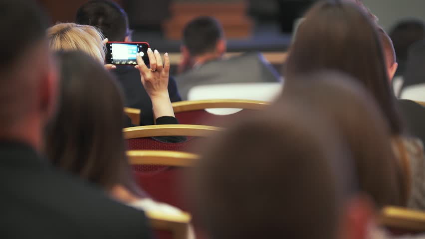 Rear view of woman shooting on smartphone awards ceremony between people on seats