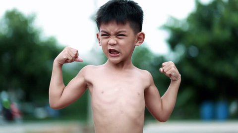 Little Asian boy shows his muscles outdoors. little boy winner sign
