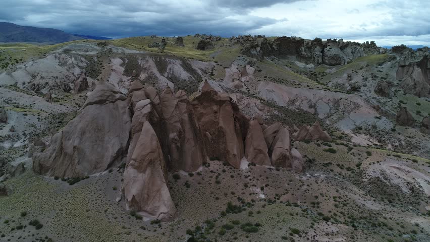 Los Bolillos, red eroded rock formation, on mountain slides of Varvarco valley. Coloured mountain at background. Aerial scene going fowards passing above the strange formations towards rocky landscape
