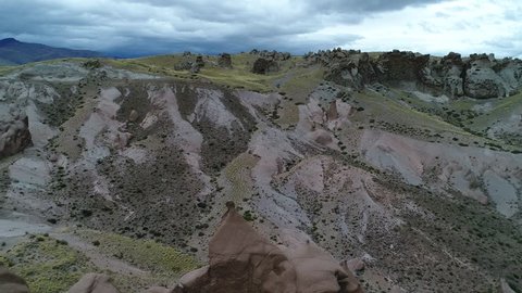 Los Bolillos, red eroded rock formation, on mountain slides of Varvarco valley. Coloured mountain at background. Aerial drone scene going backwards discovering the strange formations. Patagonia