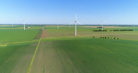 Aerial view of green crops on countryside field with rows and white Wind Turbine on horizon, agriculture industry