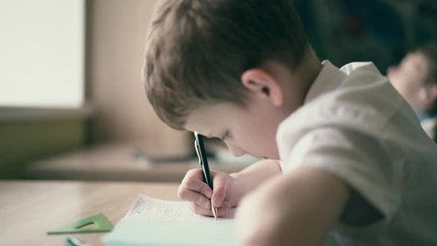 CU: Children do their homework, one sits at the table with notebooks, the second - sits in headphones, closing his eyes and listening to an audiobook, or sleeping. 