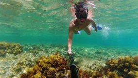 Young man swimming with snorkel and shooting underwater video about himself by his action camera