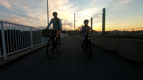 A woman on an electrical bicycle and her son crossing the bridge Alviksbron in Stockholm at sunset
