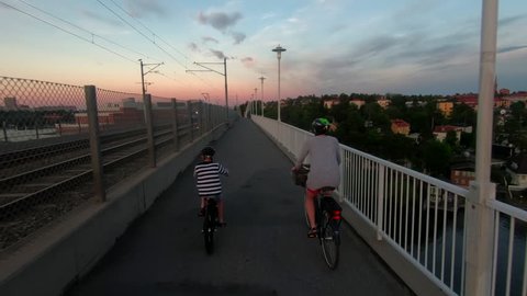 A woman on an electrical bicycle and her son crossing the bridge Alviksbron in Stockholm at sunset
