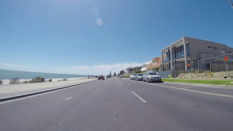 Vehicle POV, driving along The Esplanade, Henley Beach, South Australia, with views of ocean and beach, and homes overlooking the sea.