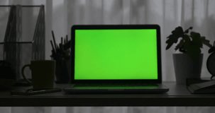 Laptop with green screen. Dark office. Dolly in. Perfect to put your own image or video.