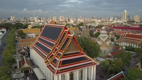 Drone shot close over Wat Phra Kaew Thai Buddhist temple Wat Pho in Bangkok. Aerial view of golden rooftops and skyline in background