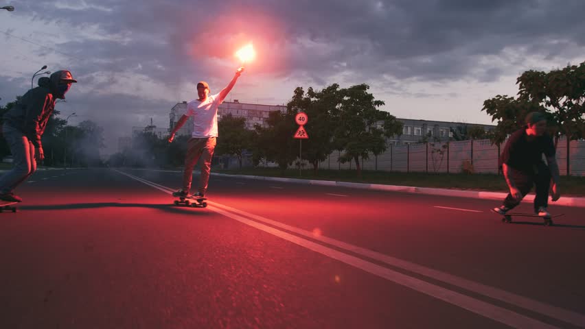 Group of young people skateboarding on the road in the early morning with red signal flare, slow motion Royalty-Free Stock Footage #1012163681