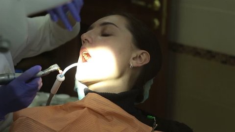 Young woman in dental clinic. Teeth cleaning. Dentist using saliva ejector or dental pump to evacuate saliva.