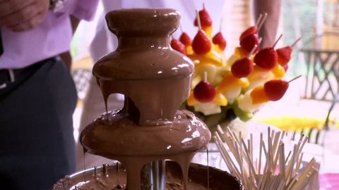 Dipping fruit skewer in raining Chocolate fondue fountain. Chocolate fondue is a natural for Valentine's day.