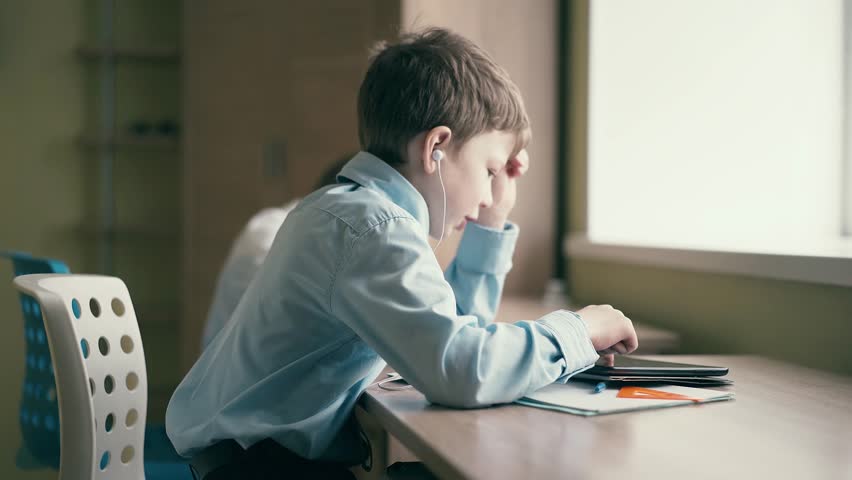 Children do their homework, one sits at the table with notebooks, the second - sits in headphones, closing his eyes and listening to an audiobook.  Royalty-Free Stock Footage #1012182938