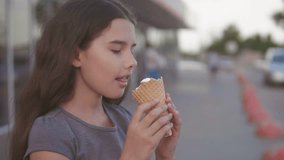 little girl eating ice cream goes down the street in the city next to the supermarket with a soft toy motion slow motion video. girl lifestyle and ice cream urban eat concept