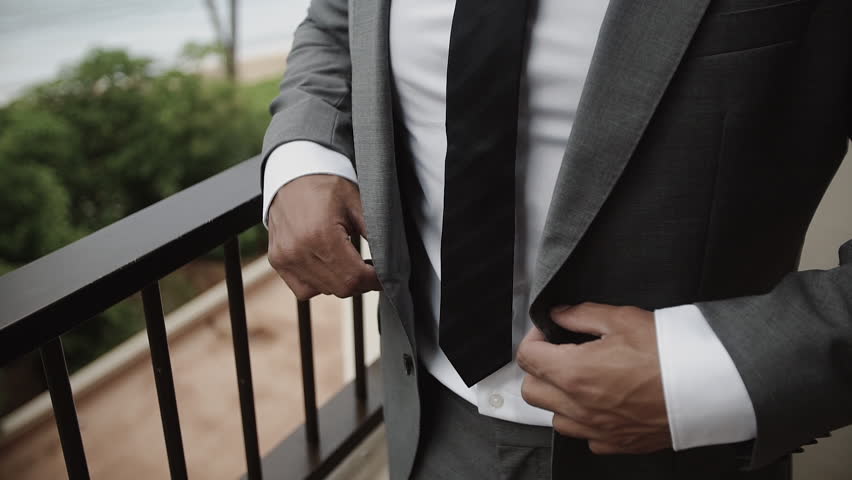 Buttoning a jacket. Stylish man in a suit fastening buttons on his jacket preparing to go out. Close up