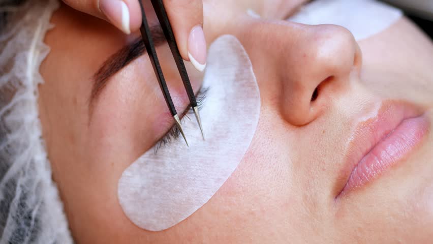Beauty saloon. close-up, procedure for eyelash extension. The master glues each cilium with special glue, works by means of two tweezers | Shutterstock HD Video #1012195913