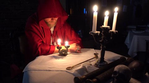 4K Mysterious monk mason sits at the table with covered face in front of candles
