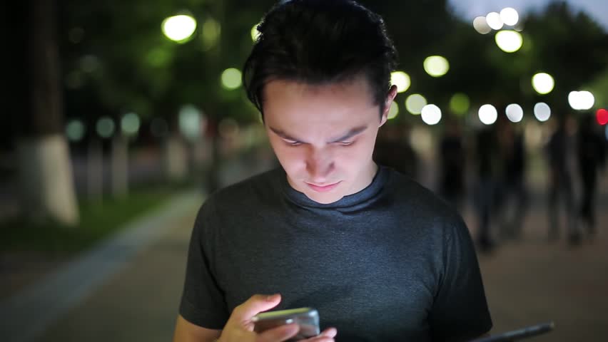 Man sms texting using app on smart phone at night in city. Handsome young business man using smartphone smiling happy. A warm summer evening.