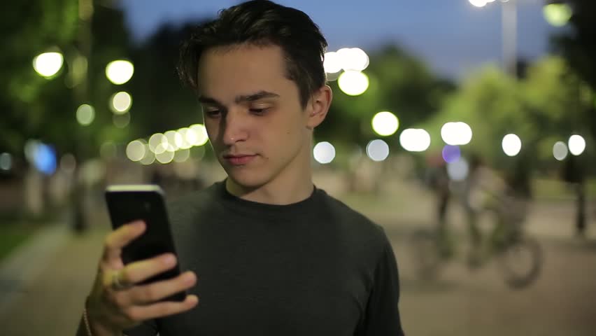 Man sms texting using app on smart phone at night in city. Handsome young business man using smartphone smiling happy. A warm summer evening.