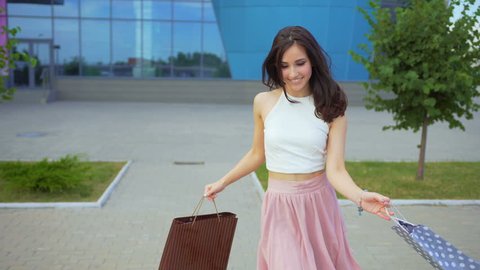 Active attractive girl dances near a shopping center with full of purchases shopping bags