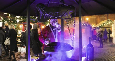 Riga, Latvia - December 18, 2017: Man In A Festive Christmas Costume Cooking Mulled Wine On Traditional Christmas Market On Dome Square.