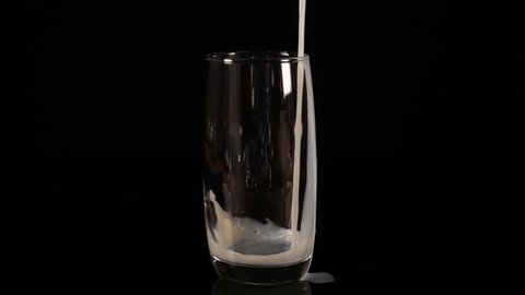 Pour milk into a glass. Slow motion. Black background.
