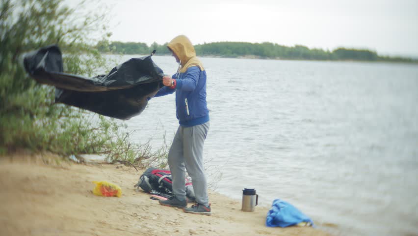 Man collects a tourist tent on the bank of the river of the sea 4k