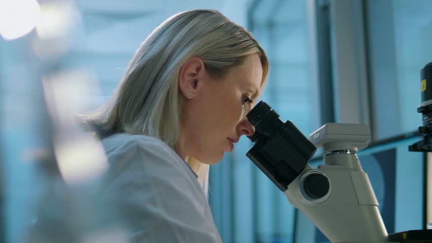 Young life scientist looking through a microscope in a laboratory. | Shutterstock HD Video #1012236620