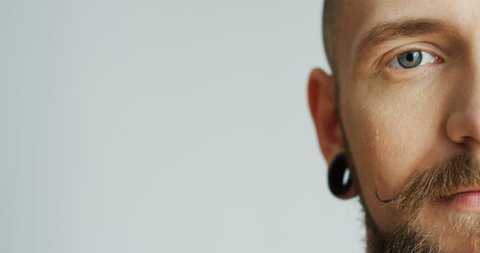 Close up of the attractive male hipster half face with earings smiling and looking at the camera. White wall background. Portrait. Inside.