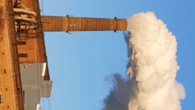 Factory plant smoke stack over blue sky background. Energy generation and air environment pollution industrial scene. Vertical format video.