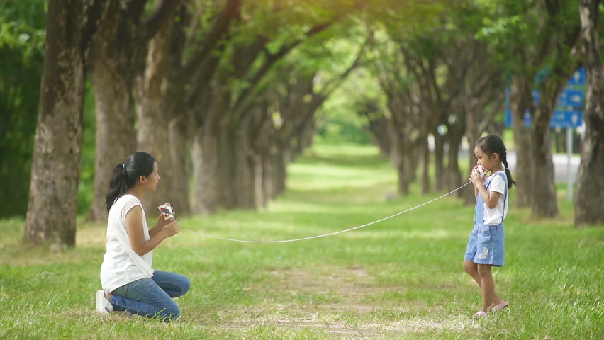 Asian family, mother and daughter doing string phone play activities tie rope at the park.
