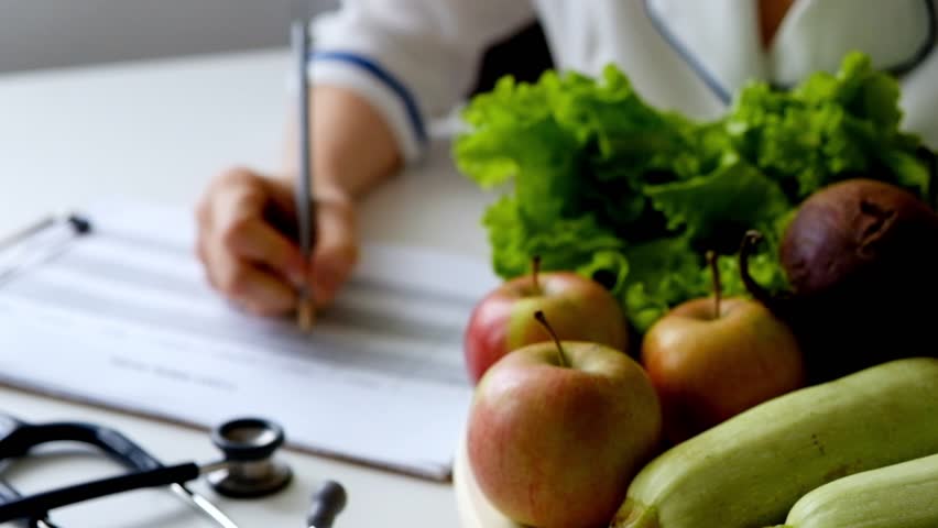 Nutritionist woman writing diet plan on table full of fruits and vegetables | Shutterstock HD Video #1012247141