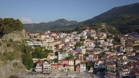 Greek village and homes by the sea. Aerial drone view of Parga on a warm summer morning. Narrow streets on hills in Greece. revealing background bay with anchoring boats