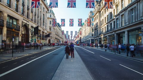 LONDON, UK - 19.05.2018: Traffic in London, Regent Street with pedestrians, Red Buses and black Cabs passing by. Daylight before sunset, street is full of British Flags.