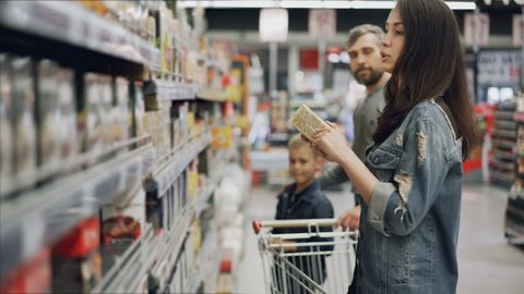 Young woman is choosing tea in food store, her husband and son are helping her looking at products and talking. Buying food and drinks in supermarket concept.