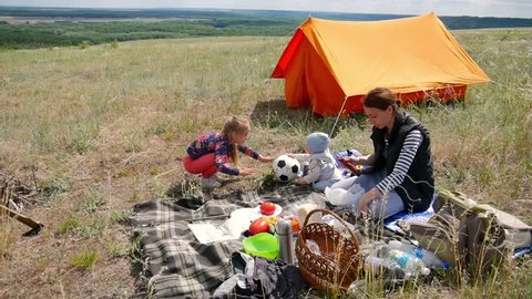 Parents and kids having a picnic and they are going to stay overnight in a tent. Traveler woman and children relaxing, playing outdoors near camping tent. Family holidays, leisure activity in forest.