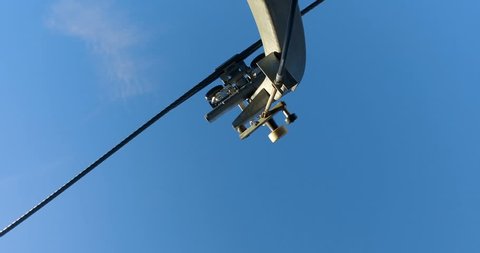 Ski lift pulley system moving against blue sky, look from below