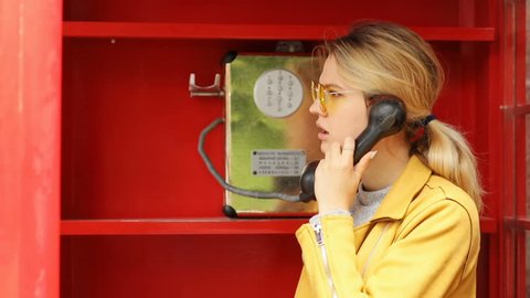 Beautiful young girl talking on the phone from the payphone disappointed sad worried woman using public telephone calling booth english britain old-fashioned style of communication on distance