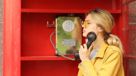 Portrait of handsome upset blonde woman finish talk on public payphone in red telephone box and going away worried unhappy face stylish female in cool sunglasses heard bad news sunny day light