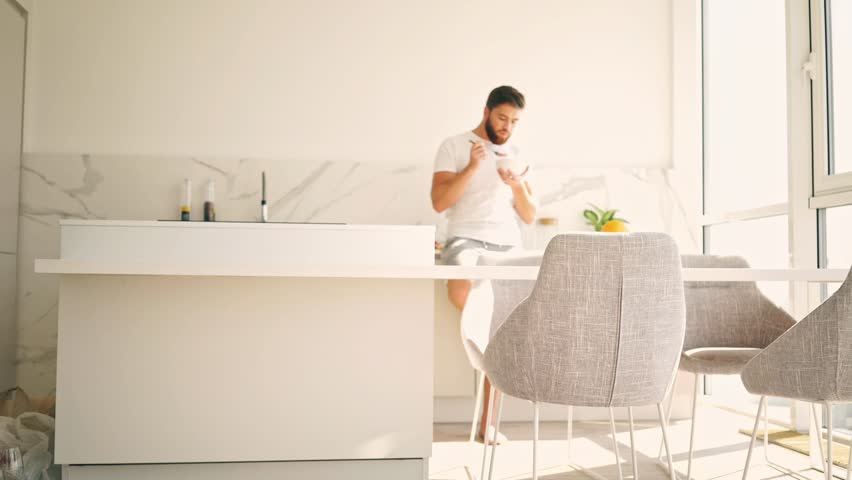Smiling bearded man standing on kitchen and eating while looking away