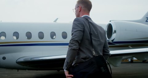 Businessman walking towards private jet on a runaway 4k