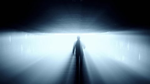 Silhouette of person walking in tunnel to the bright light.
