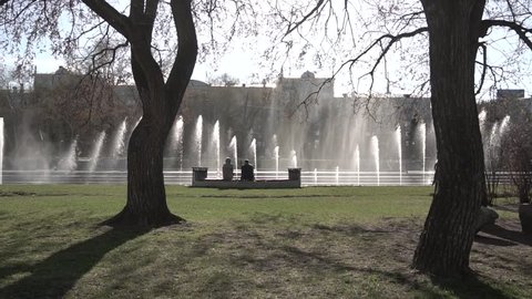 City fountain. Footage. People walking in the park. Fountain in city park on hot summer day. Stream of water, drops and bright splashes of water in beautiful city fountain