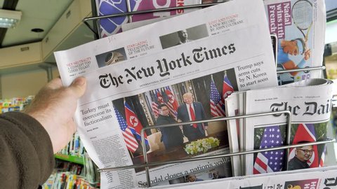 PARIS, FRANCE - JUNE 13, 2018: The New York Times on stand newspaper at press kiosk on cover U.S. President Donald Trump meeting North Korean leader Kim Jong-un in Singapore  woman walking slow motion