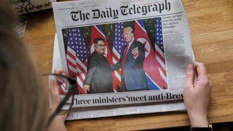 PARIS, FRANCE - JUNE 13, 2018: Woman reading The Daily Telegraph newspaper in the office showing on cover U.S. President Donald Trump meeting North Korean leader Kim Jong-un in Singapore