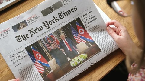 PARIS, FRANCE - JUNE 13, 2018: Woman reading The New York Times newspaper in the office showing on cover U.S. President Donald Trump meeting North Korean leader Kim Jong-un in Singapore