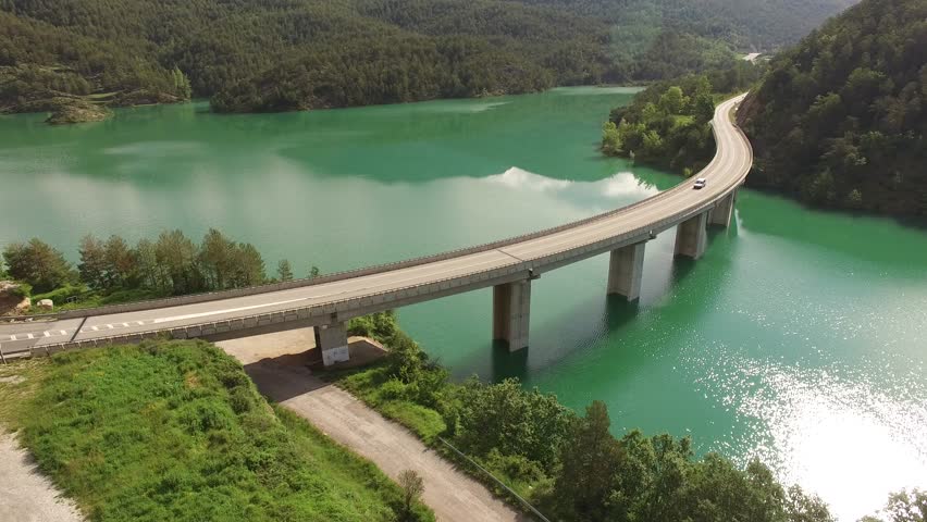 Aerial viewof bridge road curve on lake. Calm, laminated and reflective mirror water. Location, The Llosa del Cavall, c462 road, near Barcelona. Lleida Pyrenees Mountains, Catalonia, Europe