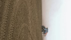 Field engine tractor seeder runs ploughs tills and plows on the field. Spring time planting seeding agricultural scene. Vertical format video.