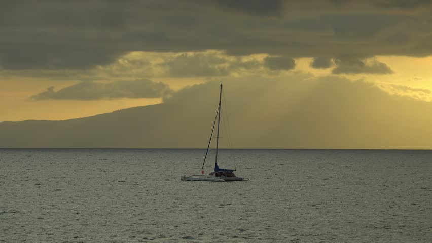 A small, modern, and anchored boat rides the gentle waves in front of a beautiful, golden sunset.